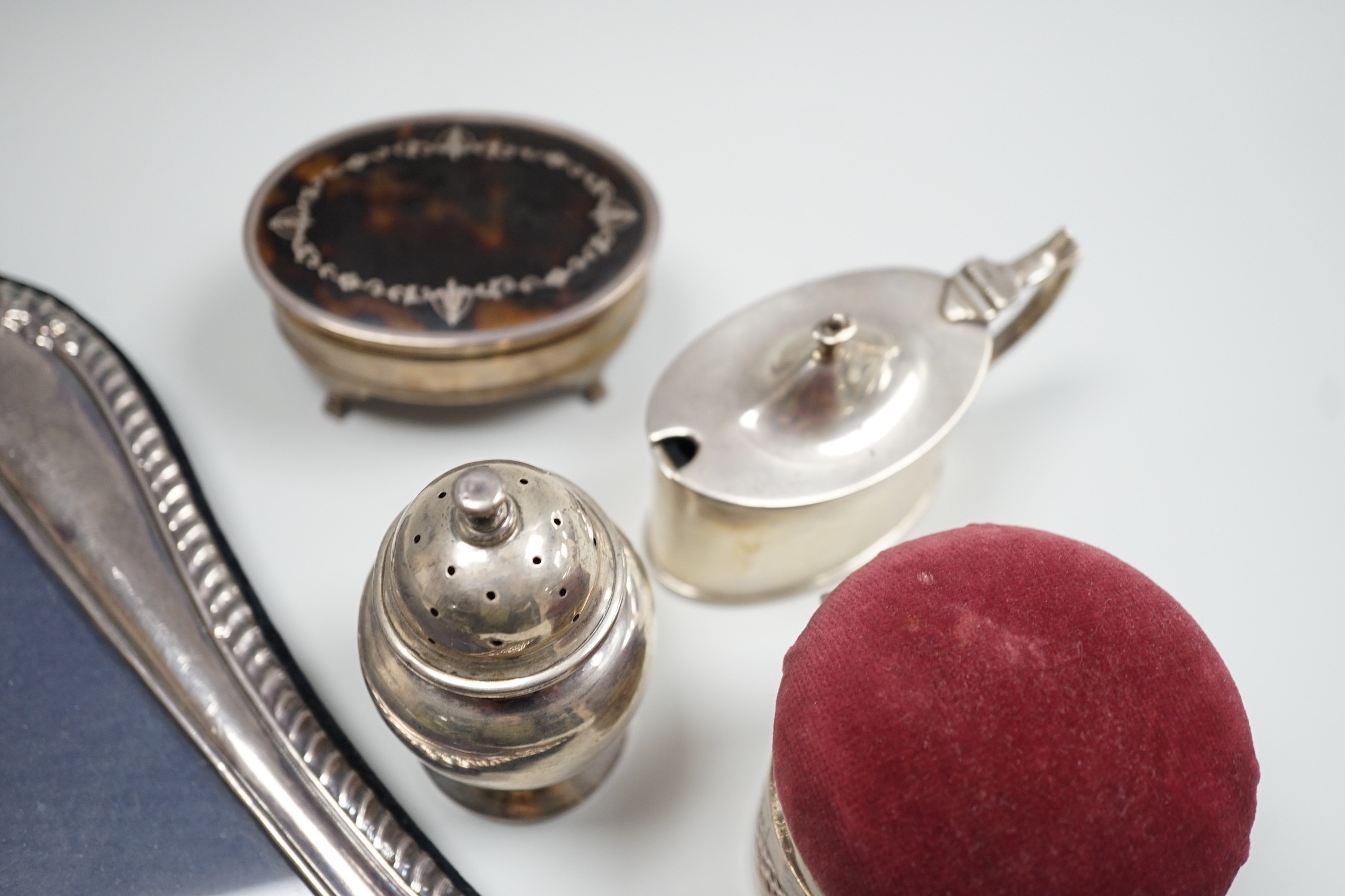 A modern silver mounted photograph frame, 30.2cm, an Edwardian silver mounted pin cushion, mustard pot, salt and a George V silver and tortoiseshell pique mounted trinket box.